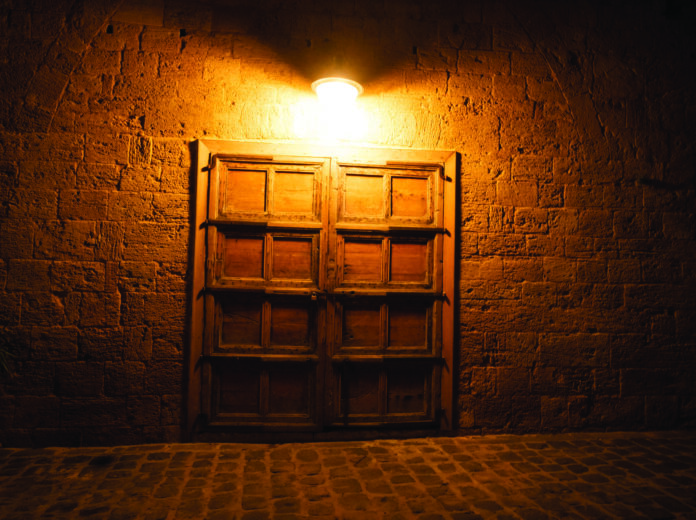 Closed,Wooden,Door,To,A,Stone,House,At,Night,Illuminated